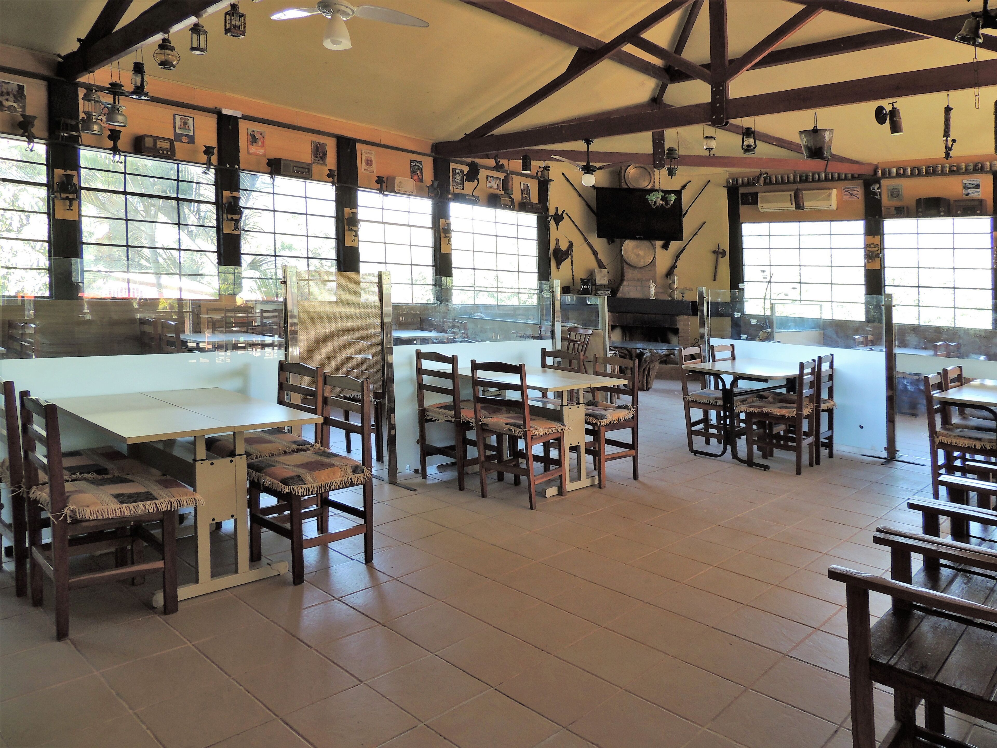 A spacious dining area with high ceilings, exposed beams, and large windows. Tables and chairs are arranged for dining.