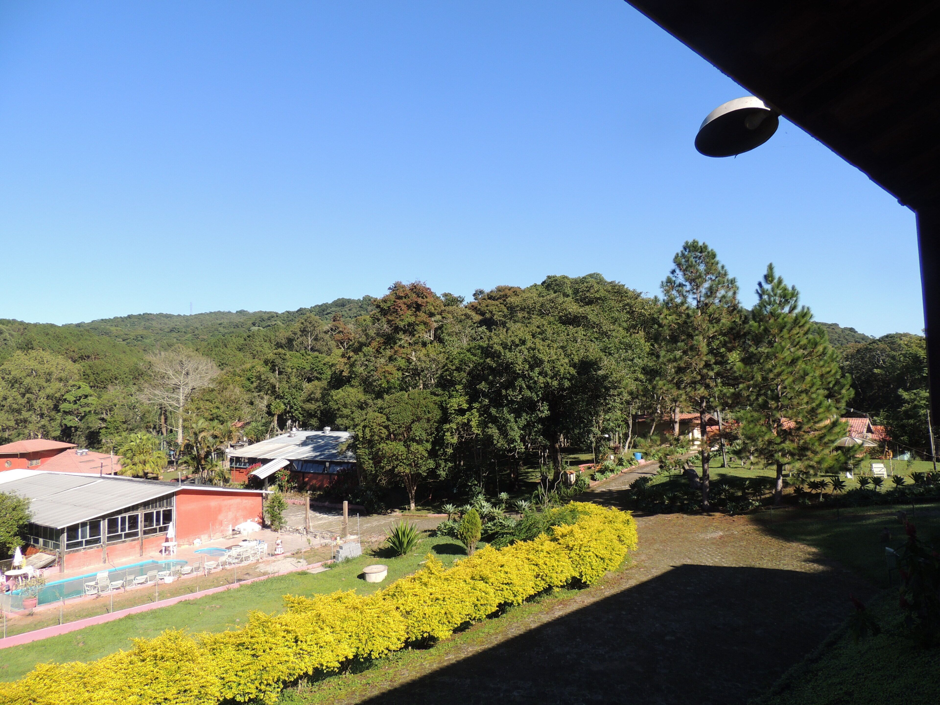 Vista de um hotel com piscina, rodeado por vegetação exuberante e colinas.