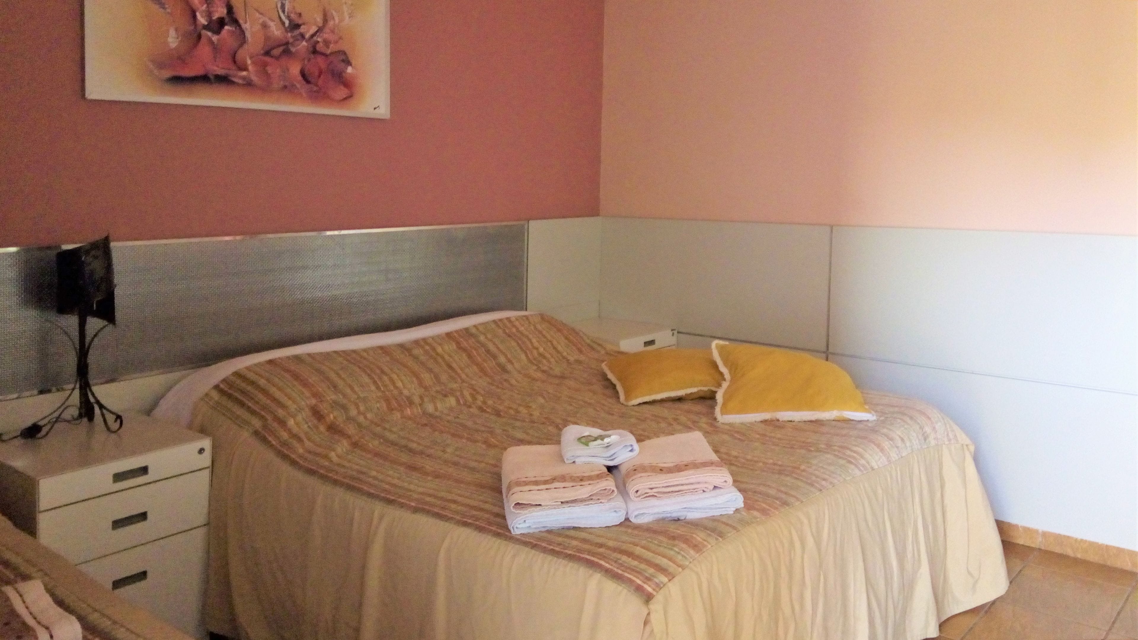 A neatly made bed with a striped blanket, two pillows, and folded towels on a headboard.