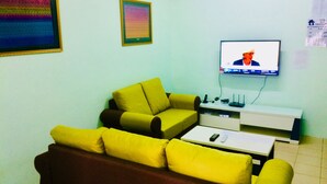 En stue med en gul sofa, en brun sofa og et hvidt sofabord. Der er et fladskærms-tv ophængt på væggen.