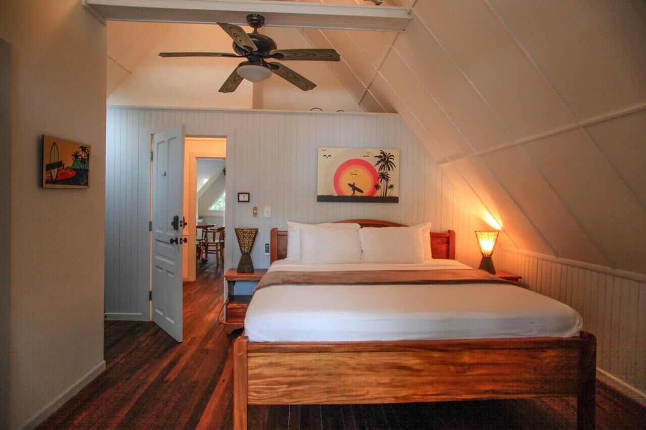 A bedroom with a wooden bed, a ceiling fan, a wall-mounted lamp, and a door leading to another room.