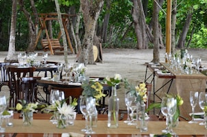 Un área de comedor al aire libre con mesas dispuestas para una comida, rodeada de árboles.