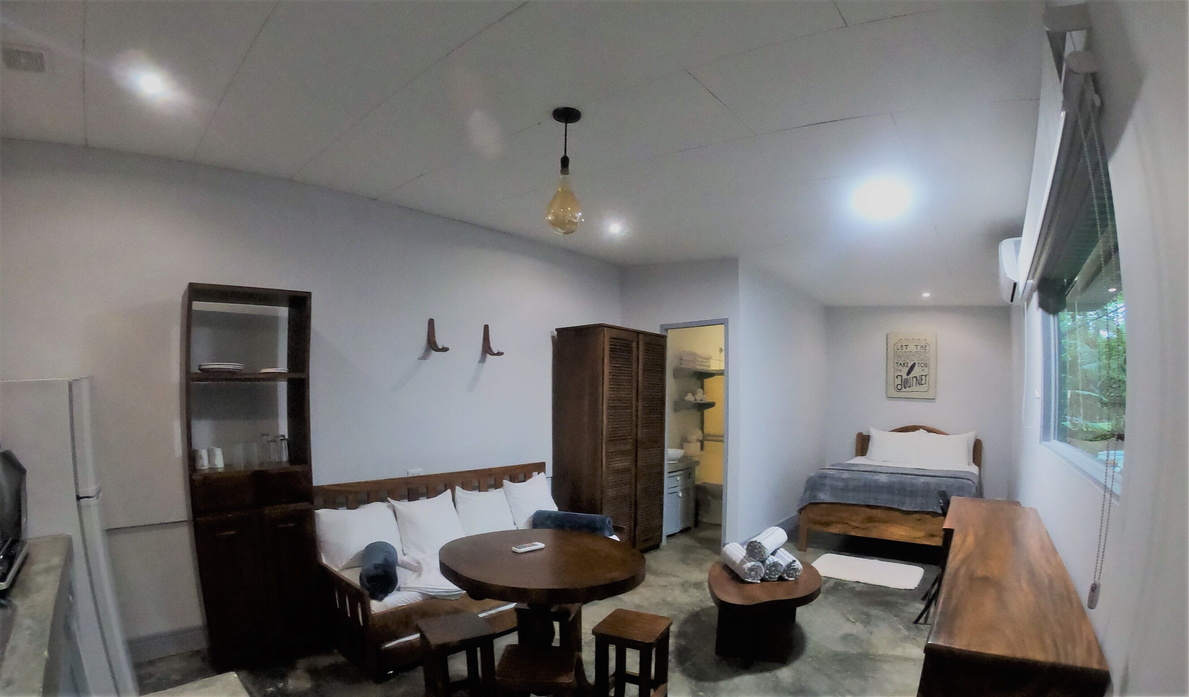 A cozy room with a wooden dining table, a sofa, a bed, and a small wooden cabinet.