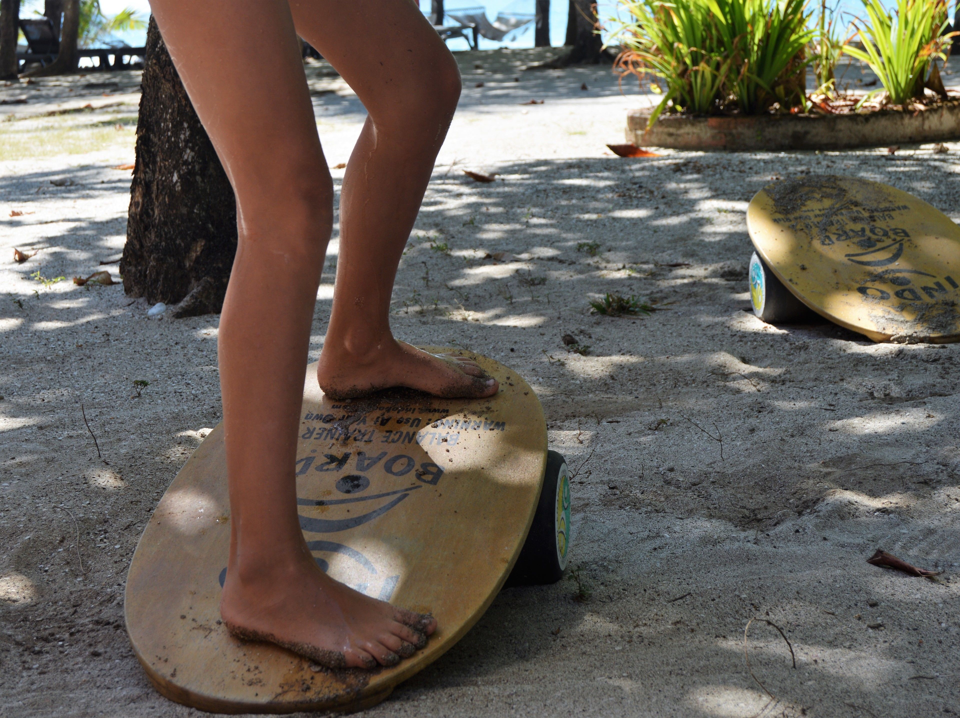 A person standing on a surfboard in a sandy area with another surfboard nearby.
