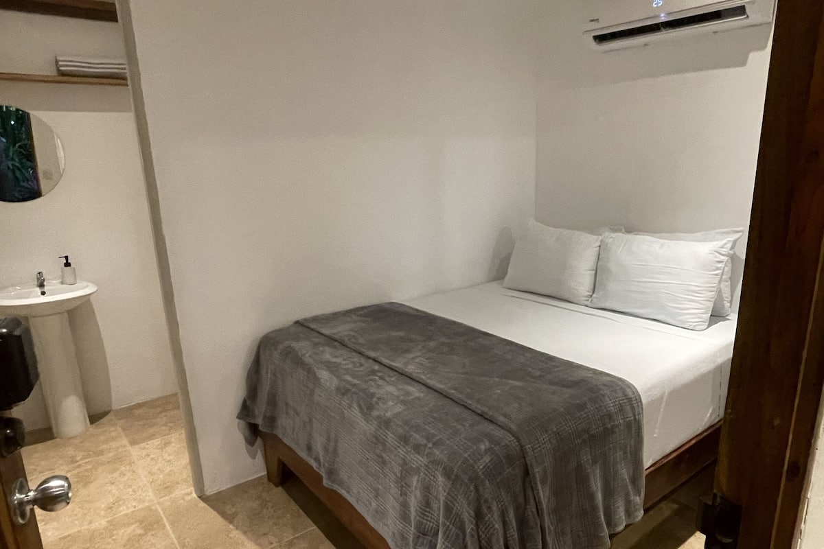 A bedroom with a bed, a bedside table, a mirror, and an air conditioning unit.