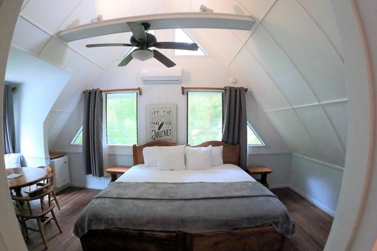 A bedroom with a bed, a desk, and a chair. There is a ceiling fan above the bed.