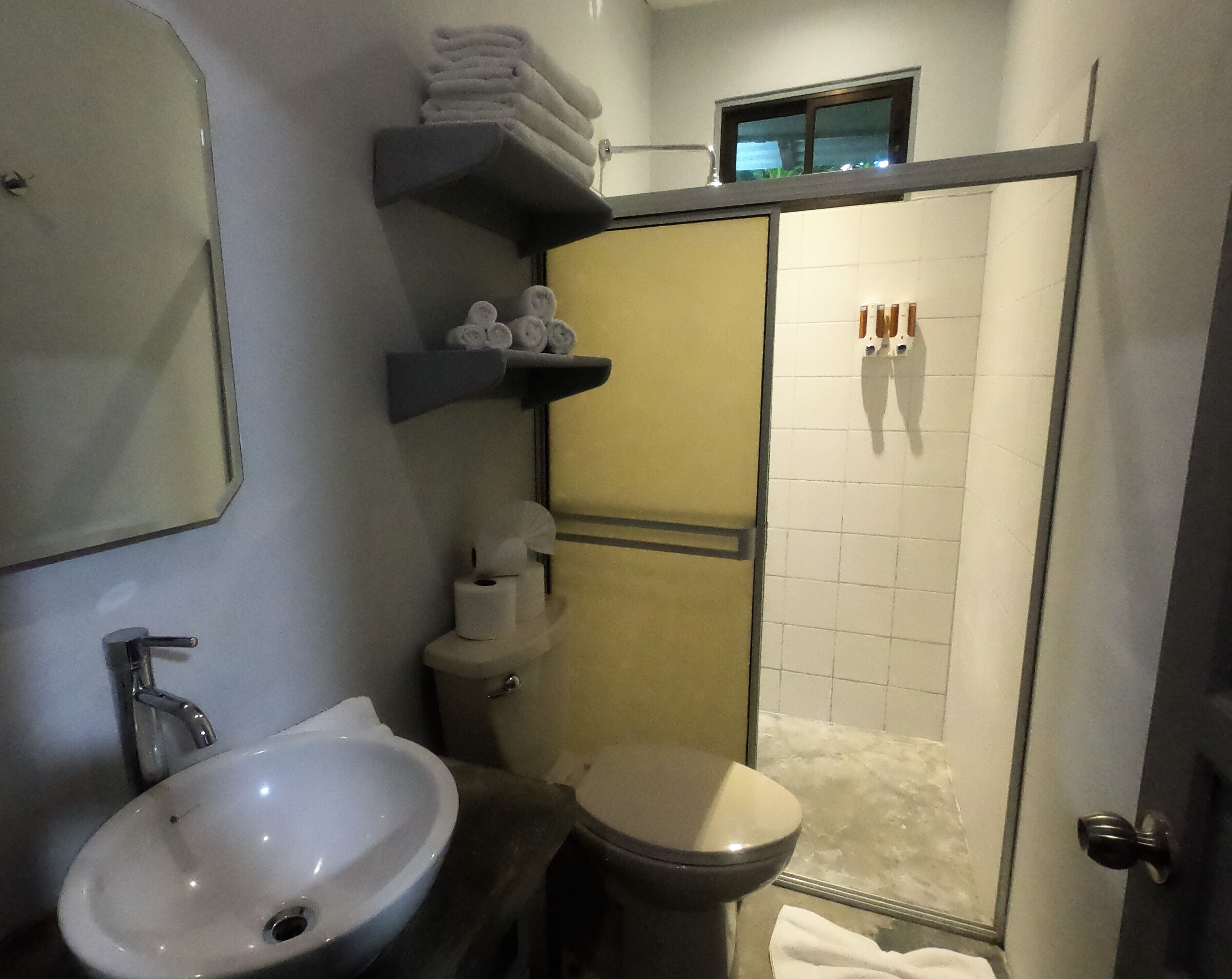 A bathroom with a sink, toilet, and shower area. There are towels and toiletries on shelves.
