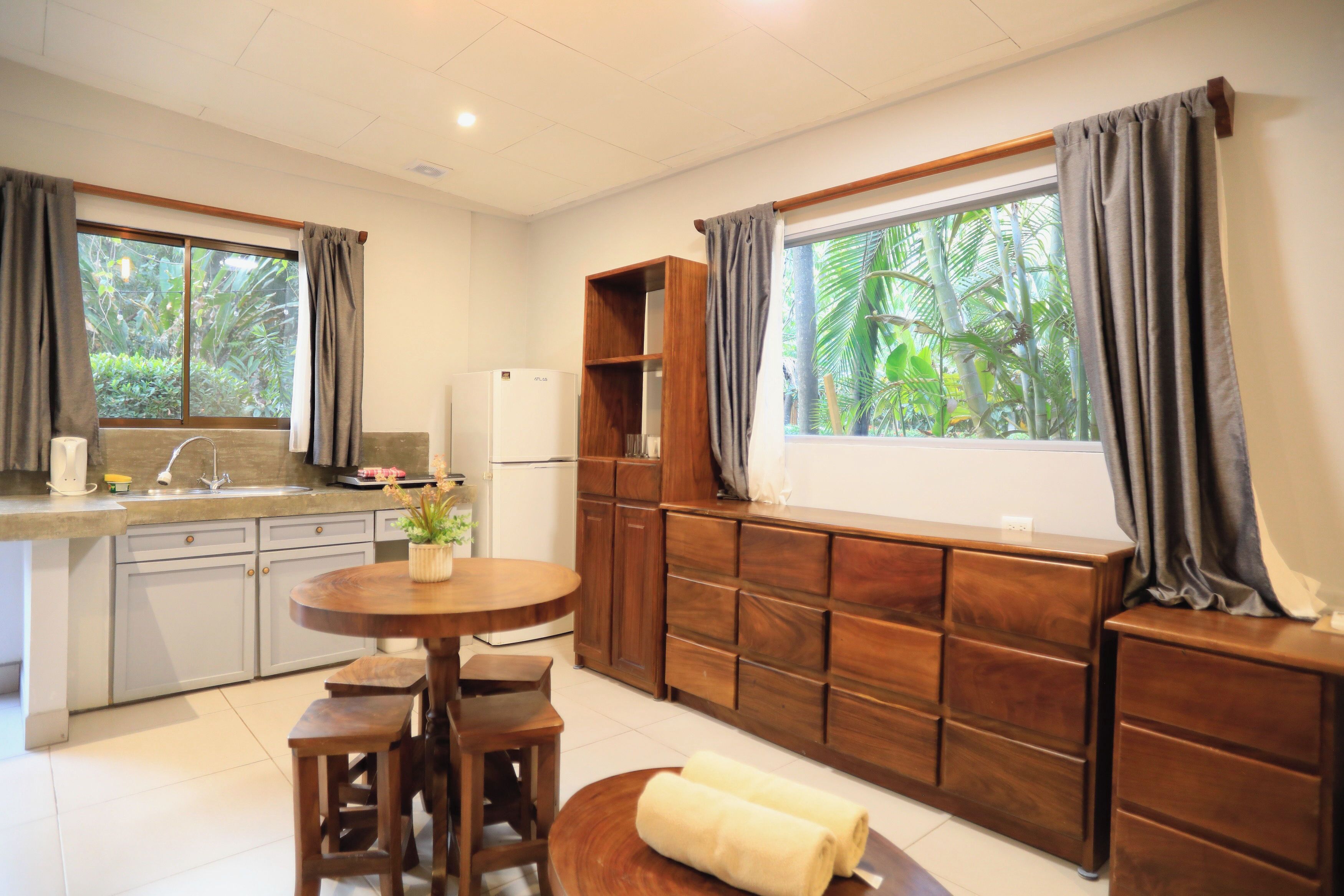 Una cocina compacta con comedor, armarios de madera, refrigerador y ventana con cortinas.