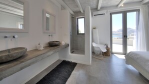 A modern bathroom with a large mirror, a stone basin, and a shower area. - Villa Nissos (Agios Vasileios)