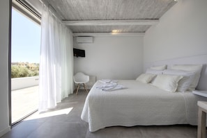 A bedroom with a large bed, a chair, and a TV on the wall.