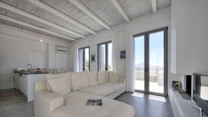 A spacious living area with a large beige sectional sofa, a flat-screen TV, and a dining area with a kitchen counter. - Villa Nissos (Agios Vasileios)