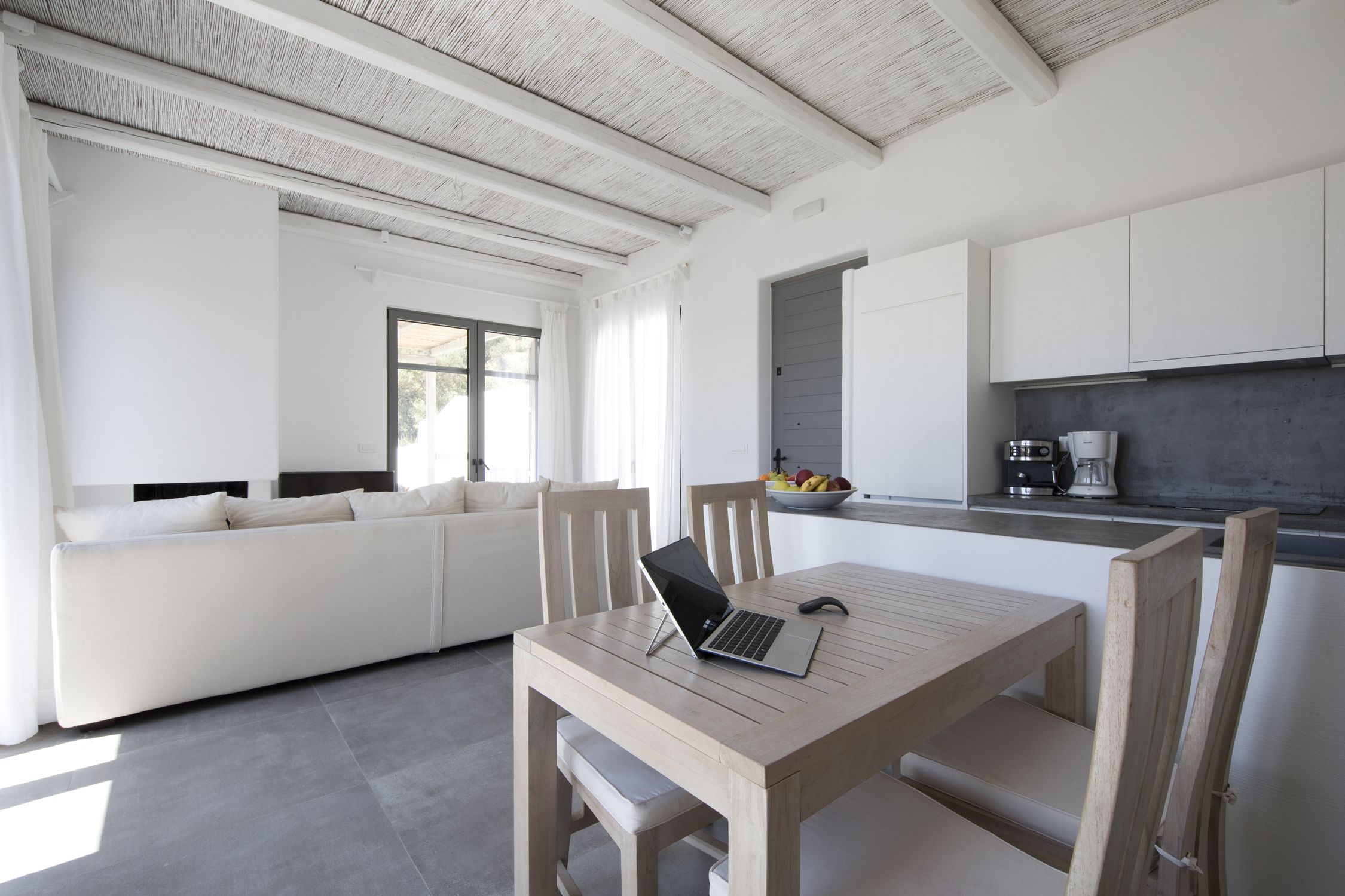 A modern kitchen with white cabinets, a wooden dining table, and a laptop on it.