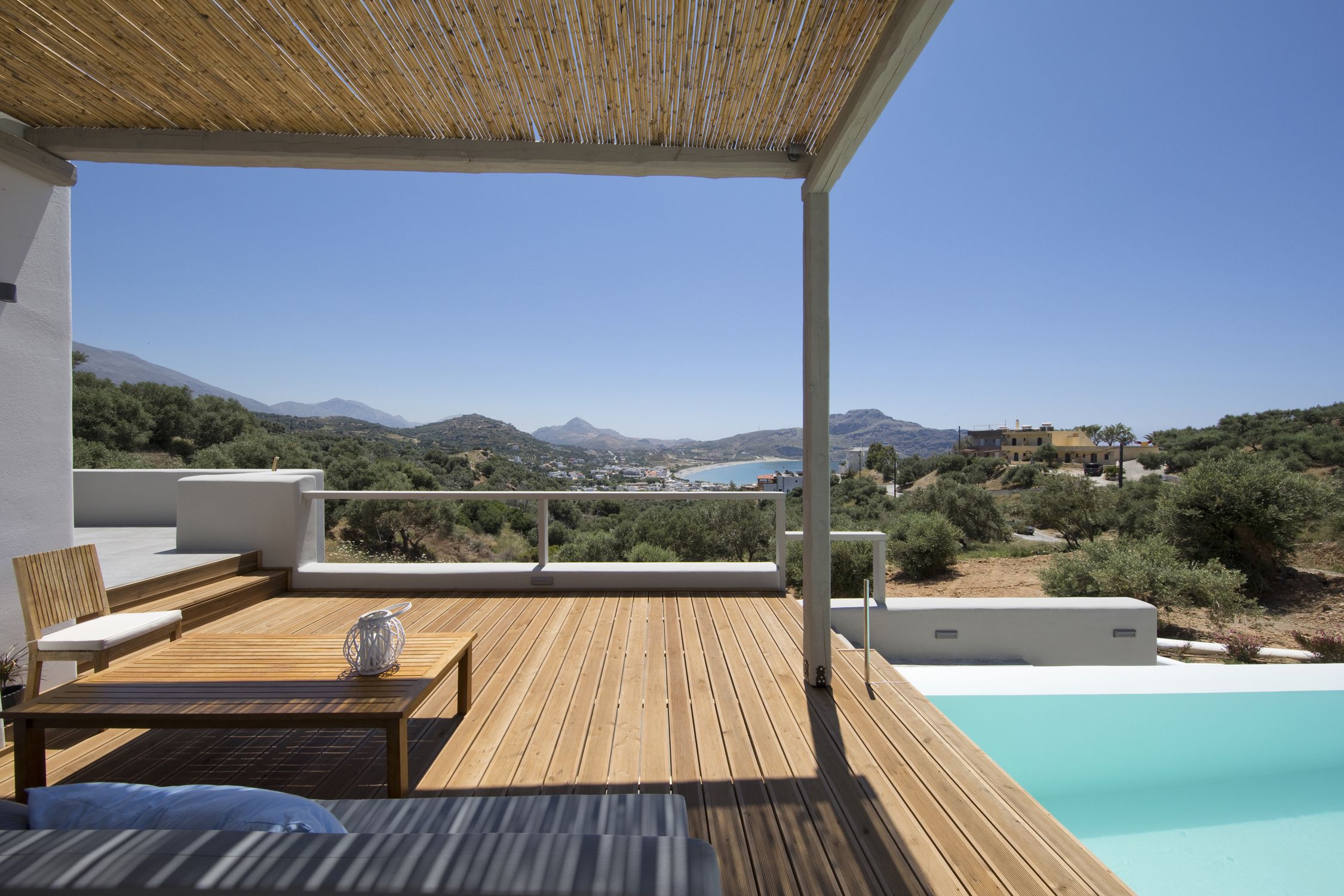 Una terraza de madera con piscina, mobiliario exterior y vistas al paisaje.