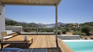 A wooden deck with a pool, outdoor seating, and a view of the landscape. - Villa Nissos (Agios Vasileios)