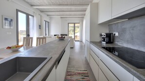A modern kitchen with a large island, built-in appliances, and a view to the outdoors. - Villa Nissos (Agios Vasileios)