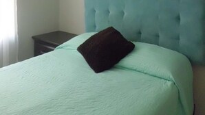 A bedroom with a single bed, a dark-colored pillow, a light green bedspread, a white air conditioning unit mounted on the wall, and a small dark-colored nightstand. - Condo Maple (Mazatlán)