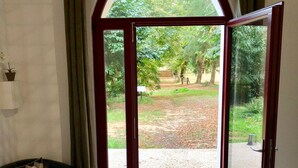 A room with a black leather sofa, a wooden coffee table, and a large arched glass door leading to an outdoor area with a gravel path and greenery. - Domaine de la Geneste (Châteaufort)