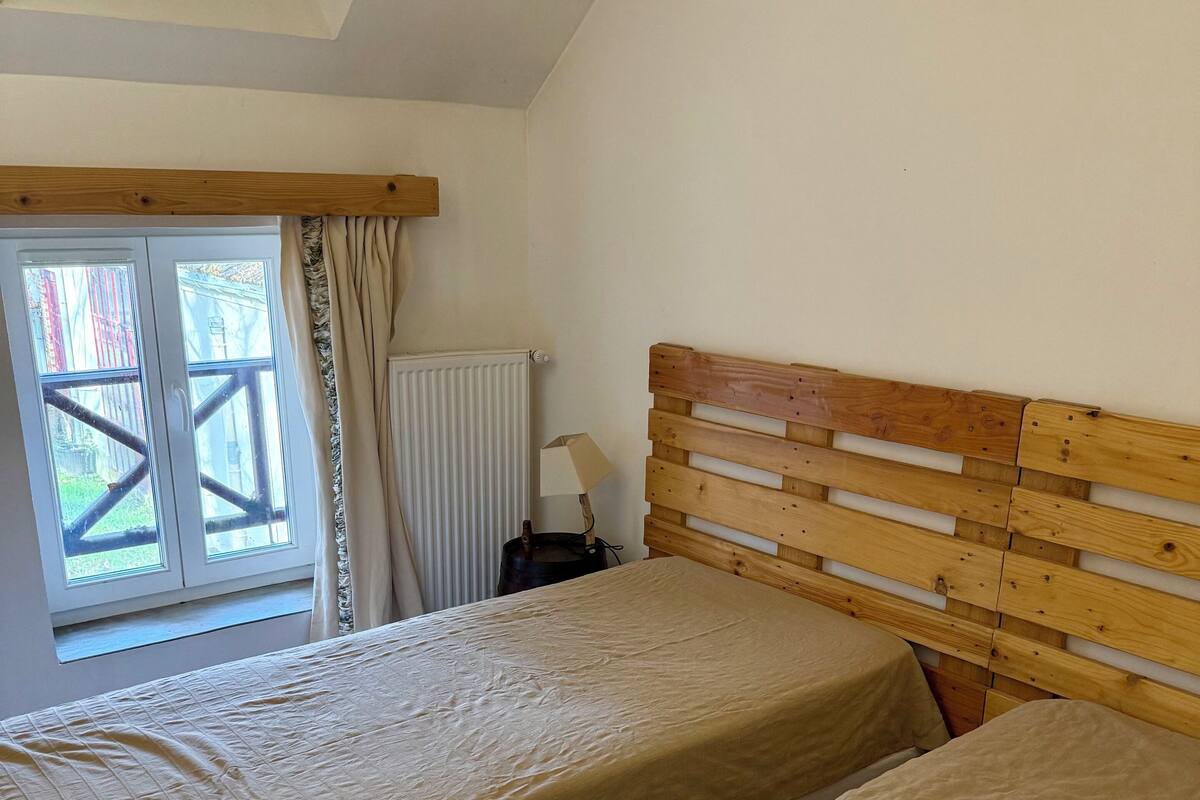 A bedroom with two beds, a wooden headboard, a window with curtains, and a radiator.