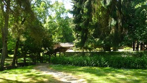 A stone pathway leading to a wooden structure surrounded by lush greenery and tall trees. - Domaine de la Geneste (Châteaufort)