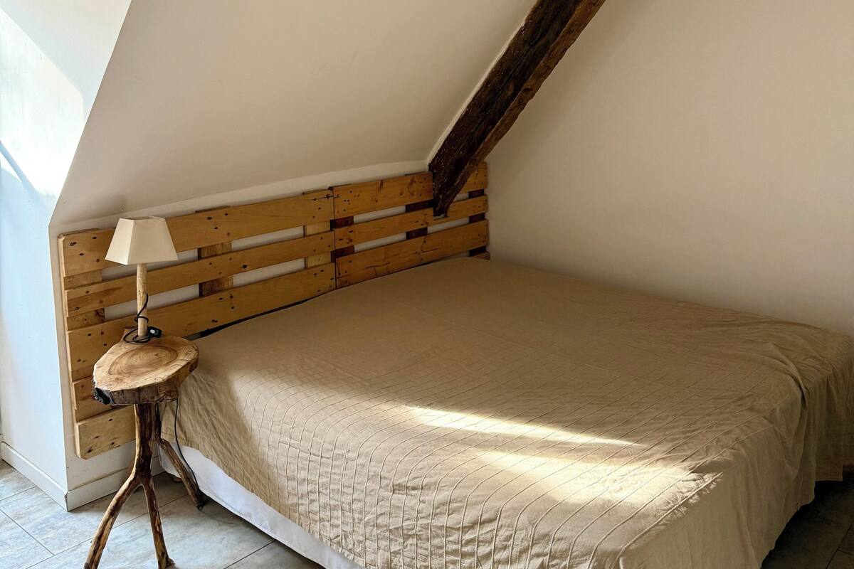 A bedroom with a sloped ceiling, a wooden headboard, a bedside lamp, and a bed with a beige quilt.