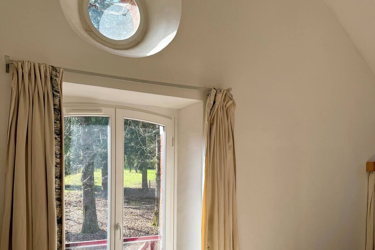 A room with a bed, a large window with curtains, a skylight, and a view of the outdoors.