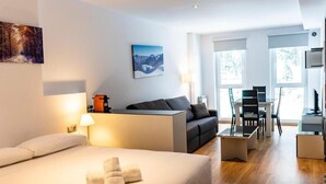 Une chambre d’hôtel moderne avec un grand lit, un canapé, un bureau et une chaise. Il y a deux fenêtres et un tableau au mur.