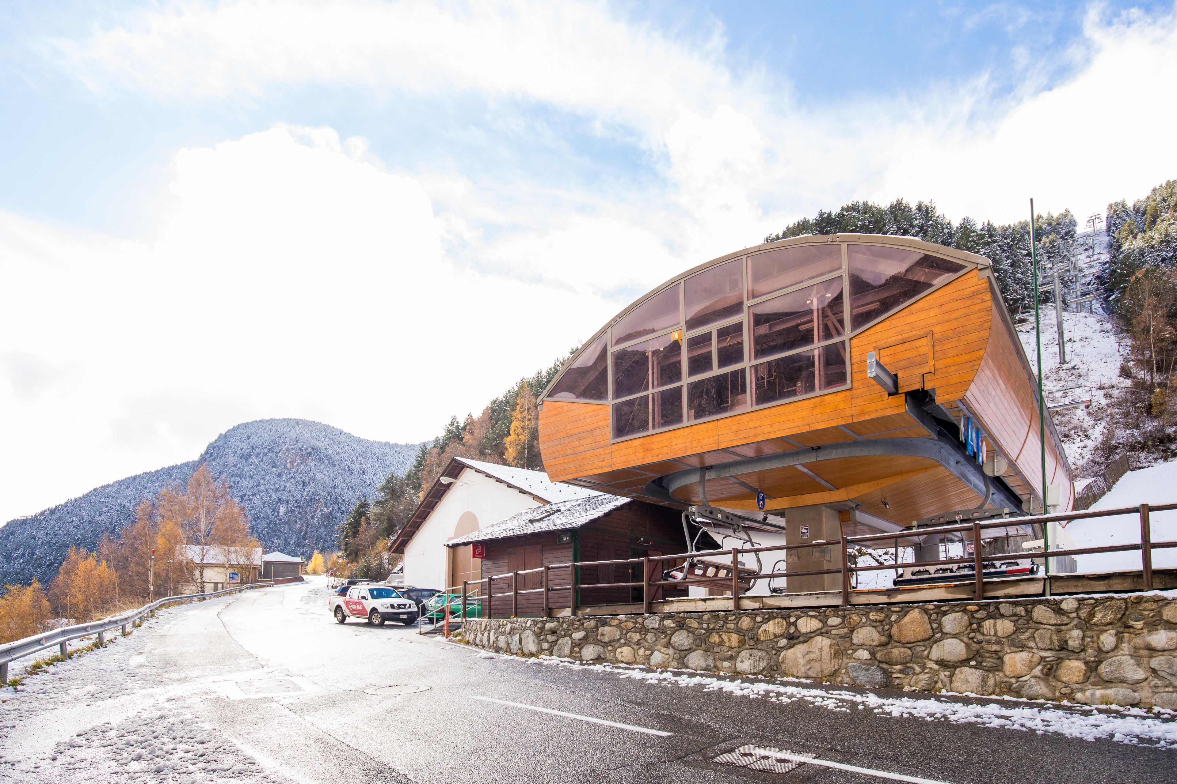 A modern building with a curved wooden facade, a stone wall, and a view of a snowy mountain.