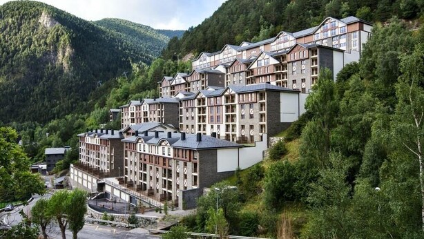 Un hôtel à plusieurs étages, de style architectural traditionnel, situé sur une colline et bordé d’une forêt.