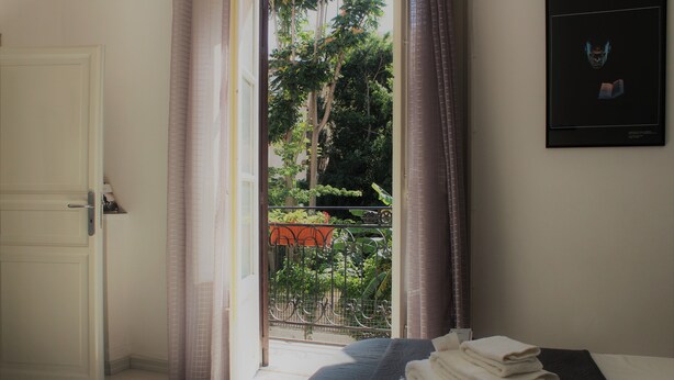 A hotel room with a bed, a door, and a view of the outside balcony. - Palazzo Cutelli LGBTQ House (Palermo)