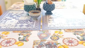 A table with a patterned tablecloth, a small vase with yellow flowers, and a decorative bowl. - Palazzo Cutelli LGBTQ House (Palermo)