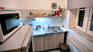A compact kitchen with a microwave, kettle, sink, and a small countertop. - Palazzo Cutelli LGBTQ House (Palermo)