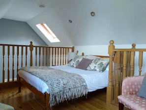 Une chambre avec un plafond en pente, un puits de lumière, un cadre de lit en bois, une chaise en bois et une balustrade en bois.