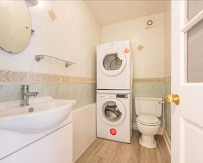 Une petite salle de bain comprenant un lavabo, un lave-linge et un sèche-linge superposés, des toilettes et un miroir.