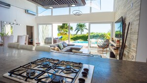 A modern kitchen with a gas stove, a dining area with a table and chairs, and a view of a pool and greenery outside. - Villas Agua Dulce (Cabarete)