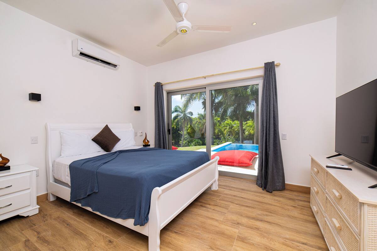 Une chambre avec un lit, une télévision, une commode et une vue sur une piscine.