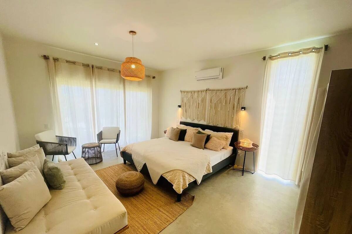 Une chambre moderne avec un grand lit, un canapé, une petite table et un luminaire suspendu.