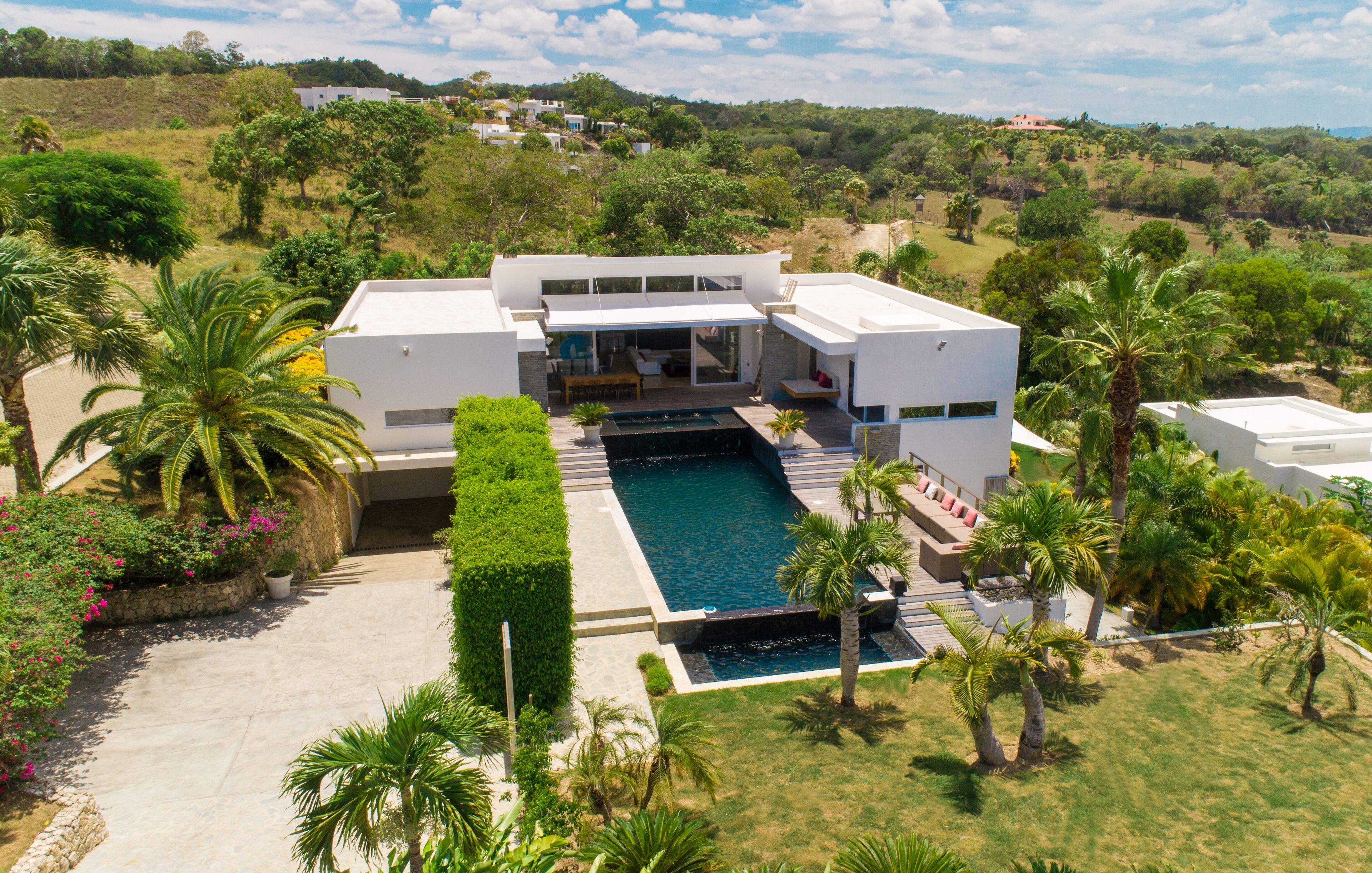 A modern house with a swimming pool, surrounded by lush greenery and palm trees.