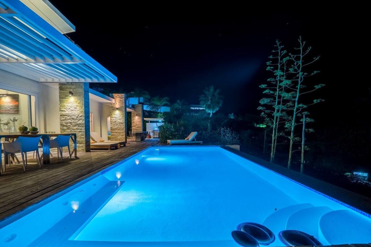 Une piscine extérieure moderne dotée d’une terrasse en bois, de chaises longues et d’un mur en pierre.