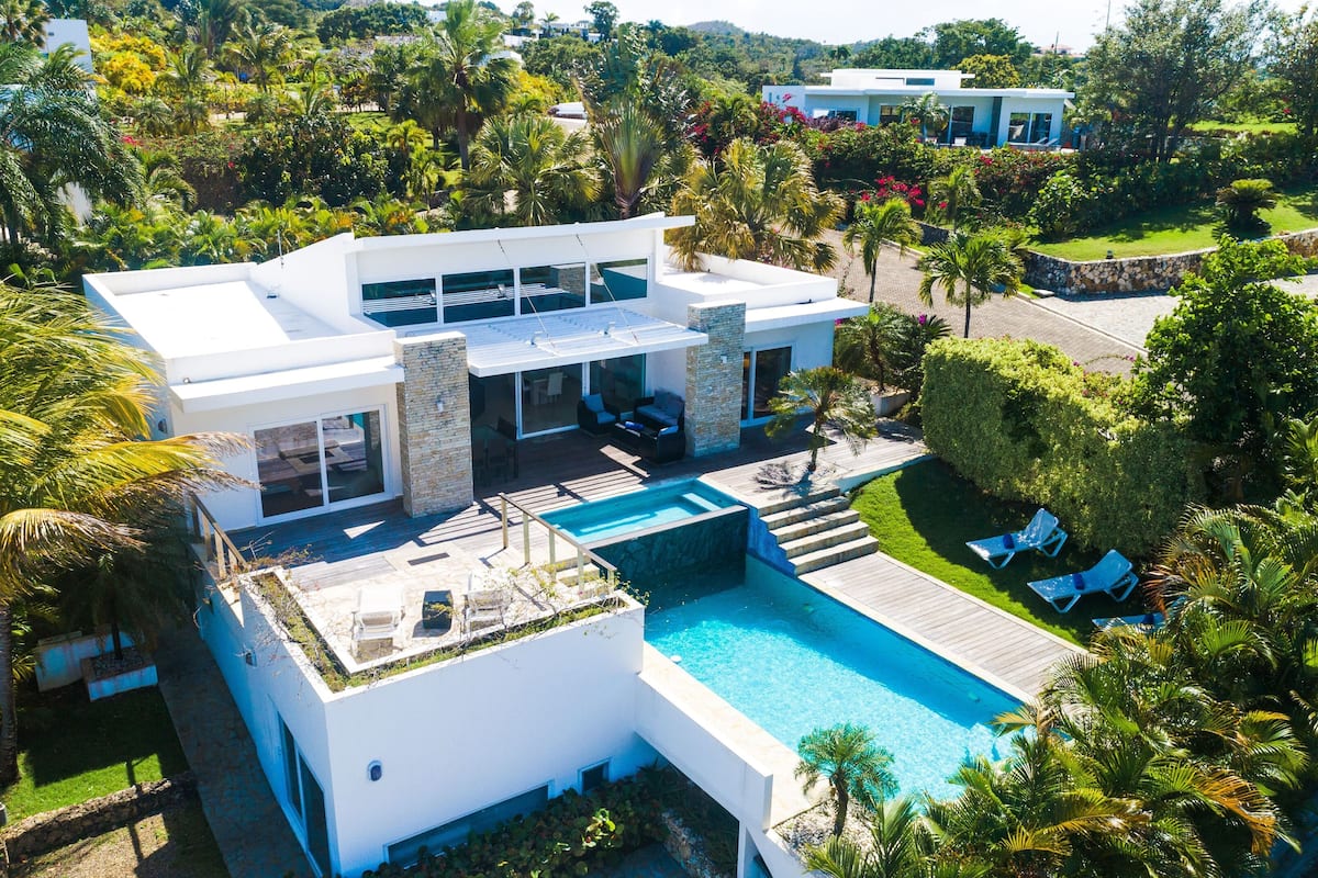 Une maison moderne dotée d’une piscine, entourée d’une végétation luxuriante et de palmiers.