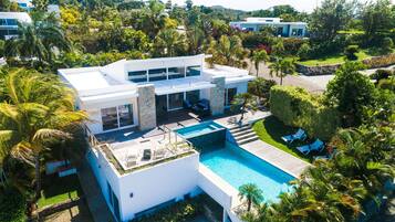 Une maison moderne dotée d’une piscine, entourée d’une végétation luxuriante et de palmiers.