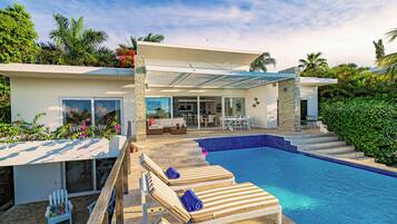 A modern house with a swimming pool, outdoor seating, and lush greenery.