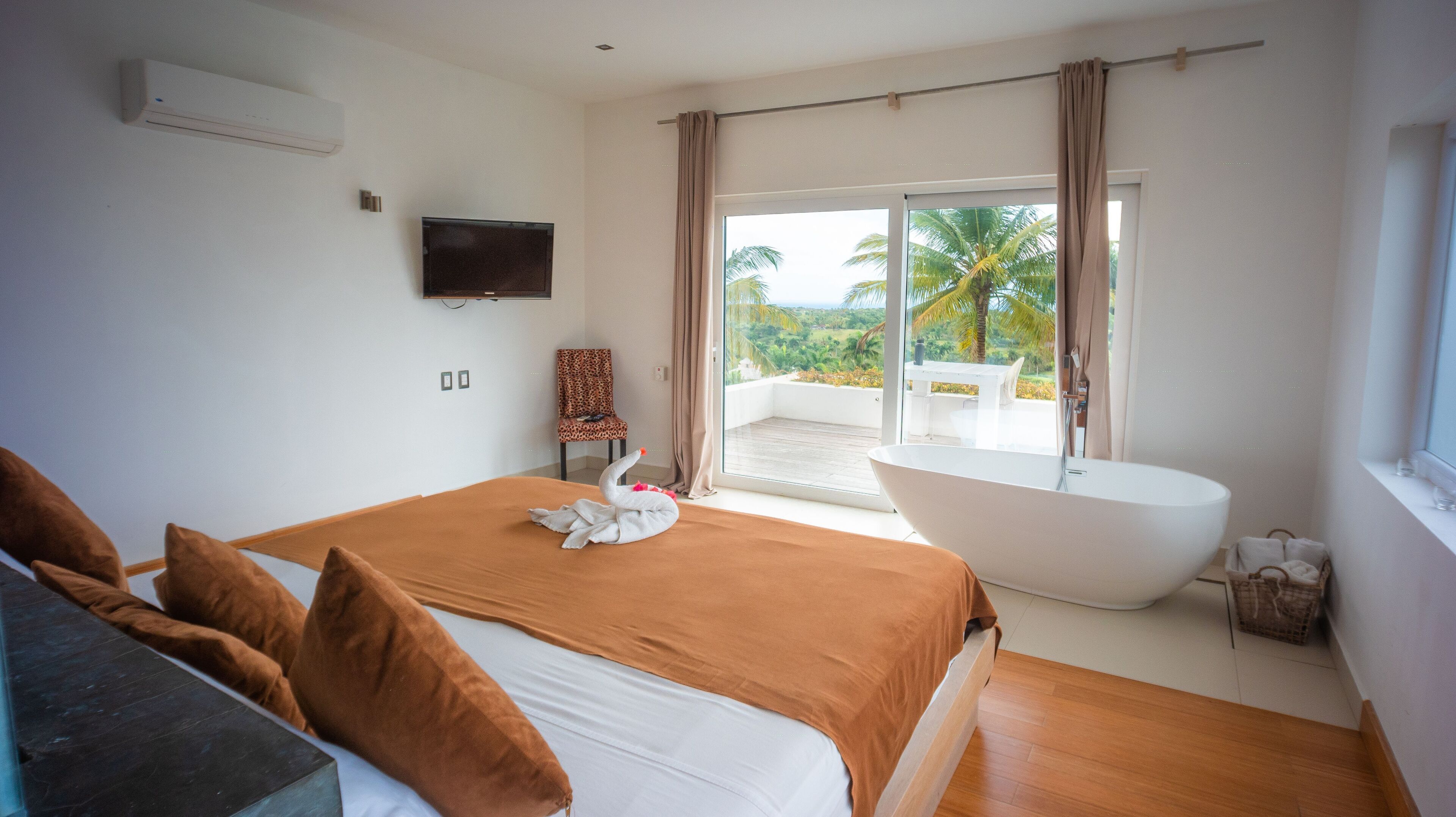 Un dormitorio con una cama grande, una bañera y un balcón con vistas a palmeras.