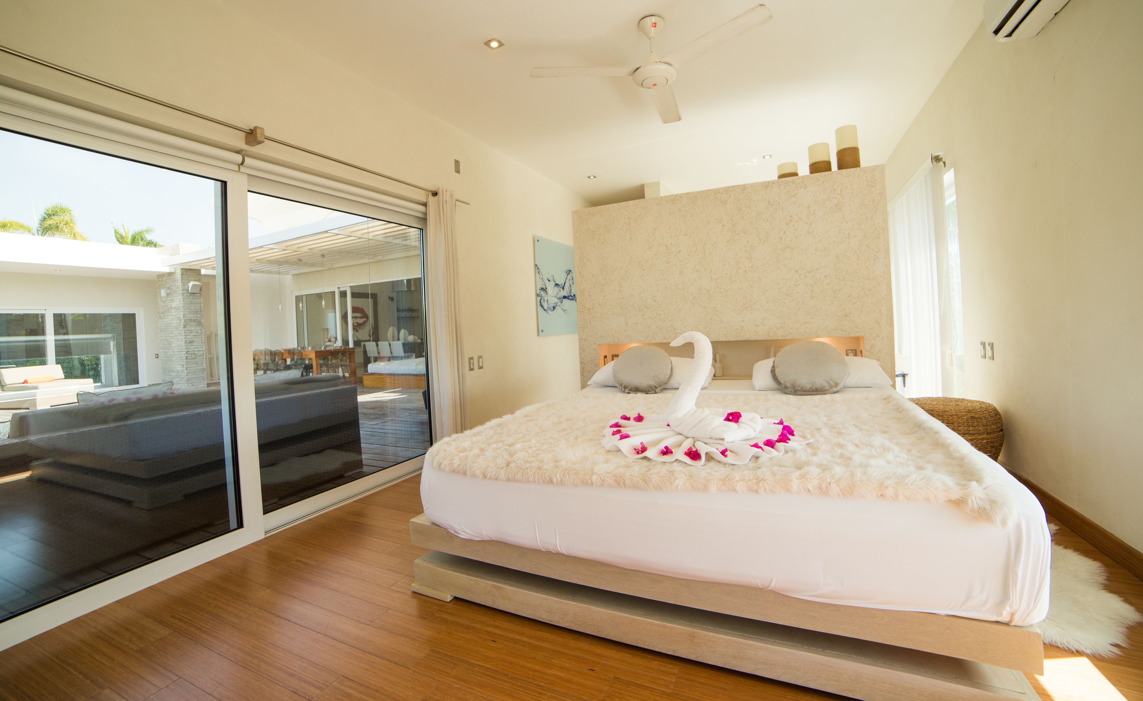 Une chambre moderne avec un grand lit, un ventilateur de plafond et une vue sur une piscine, accessible par une porte-fenêtre coulissante.
