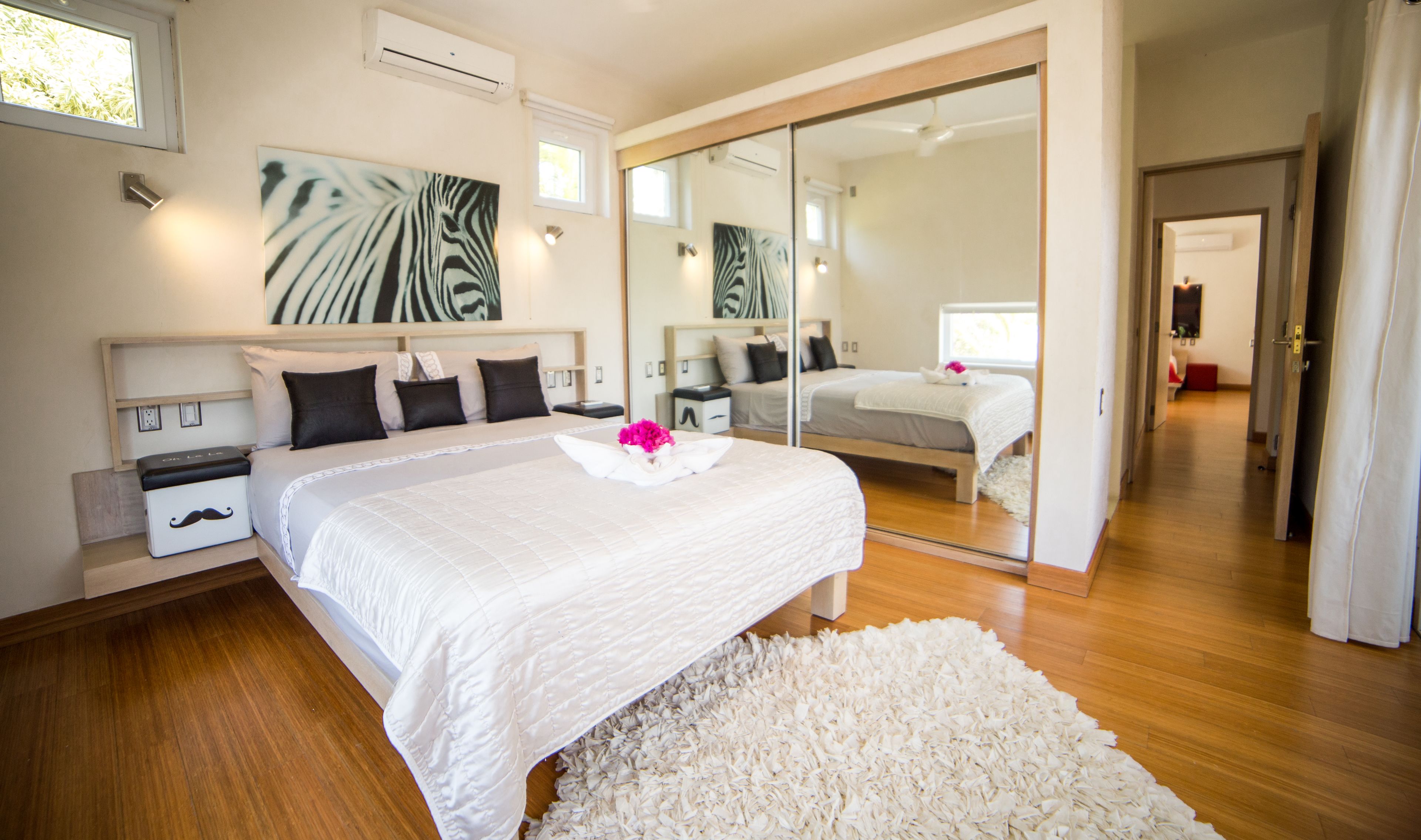 Une chambre moderne avec un grand lit, un miroir et une vue sur le couloir.