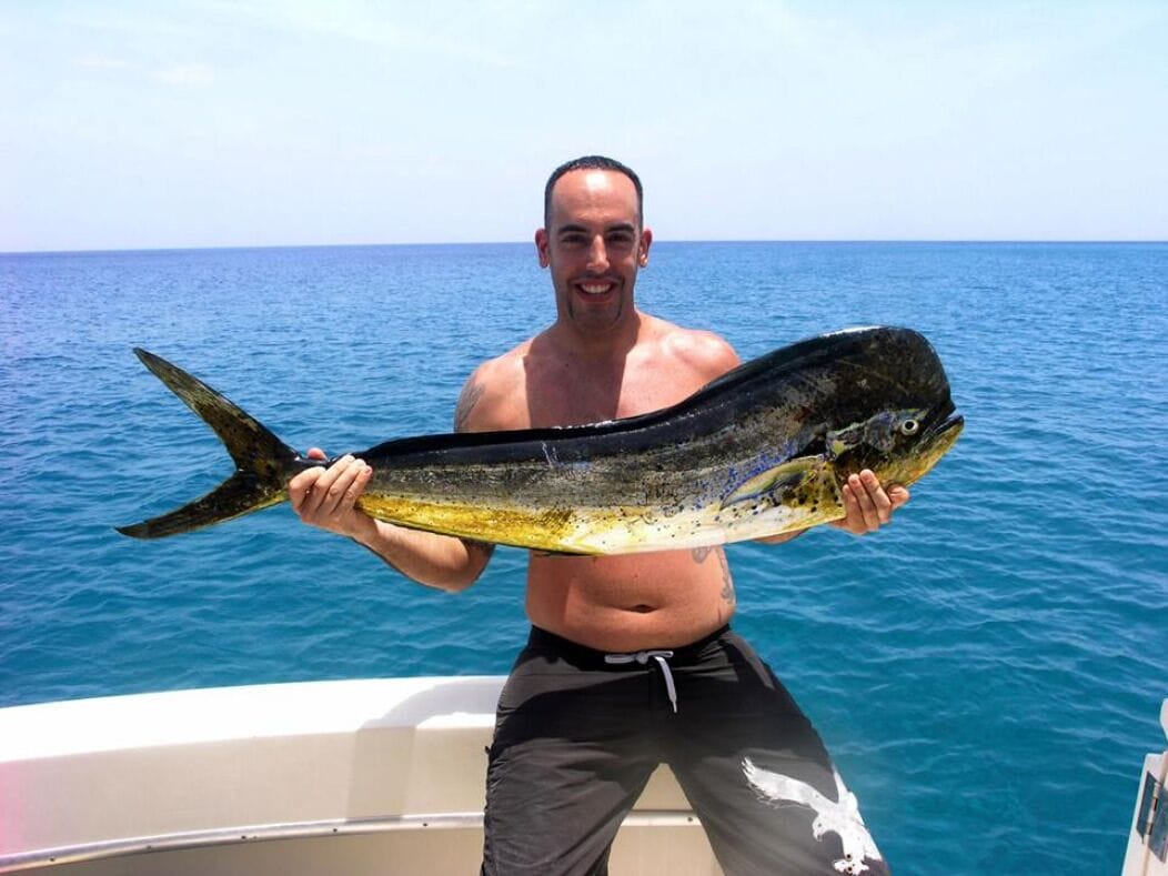 A man holding a large fish on a boat with a clear view of the ocean in the background.