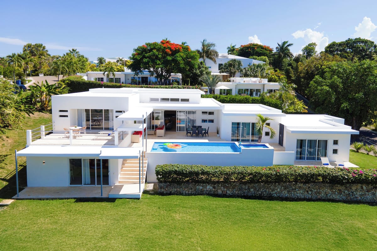Une maison moderne à plusieurs étages, dotée d’une piscine, d’un espace extérieur aménagé et d’un jardin luxuriant.