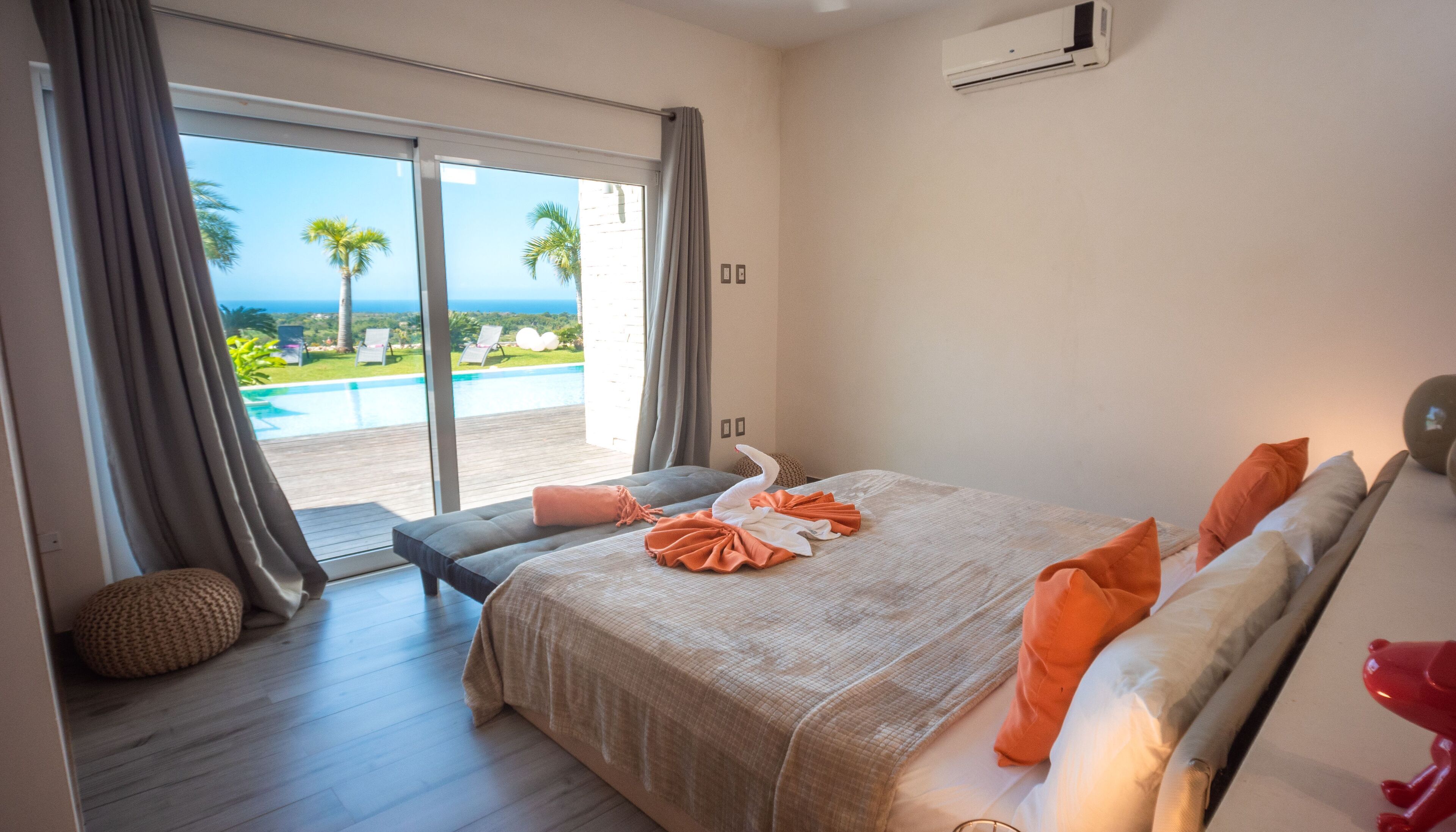 A hotel room with a bed, a bench, and a view of a pool and palm trees.