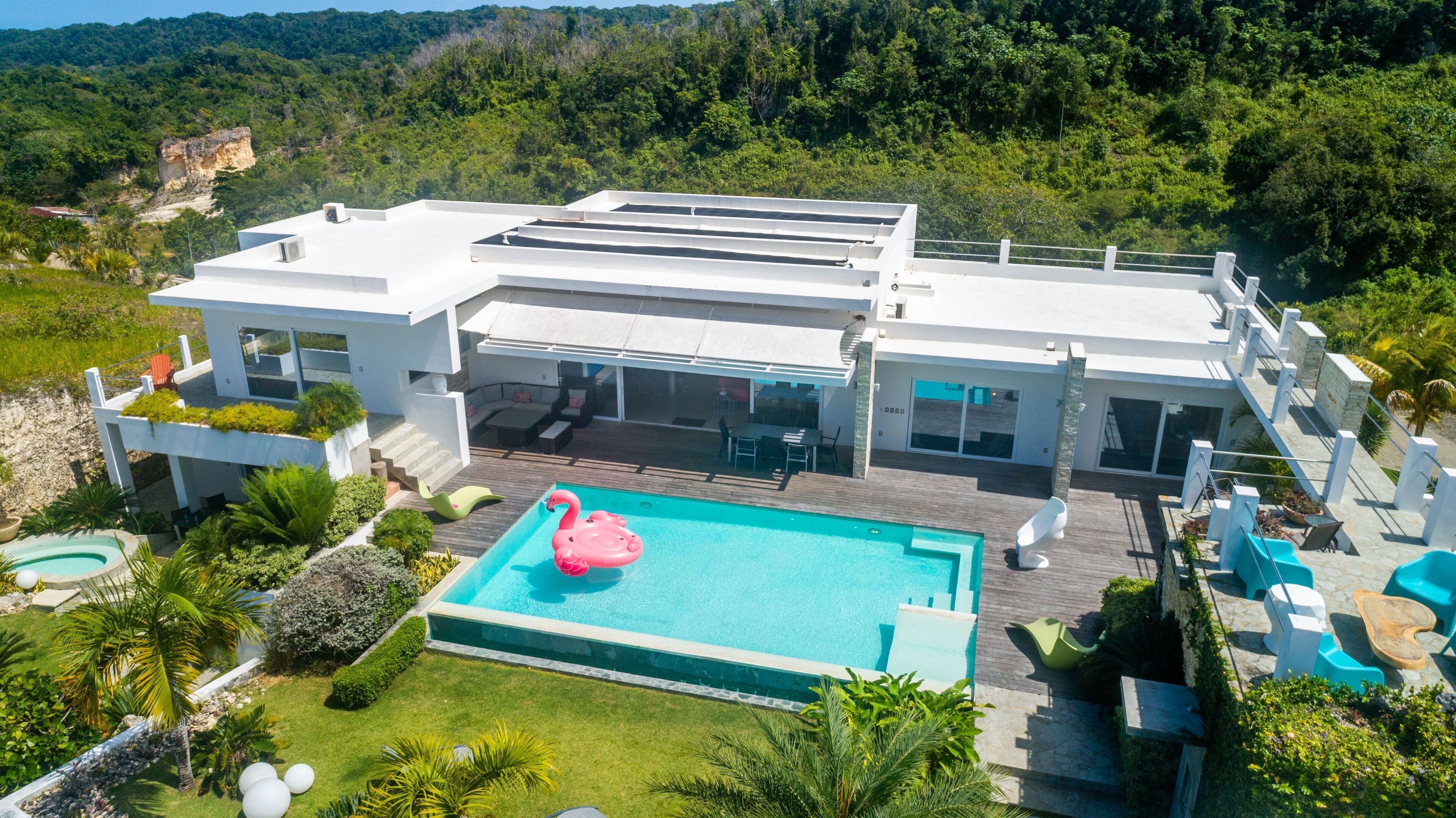 A modern house with a swimming pool, outdoor seating, and a view of the surrounding forest.