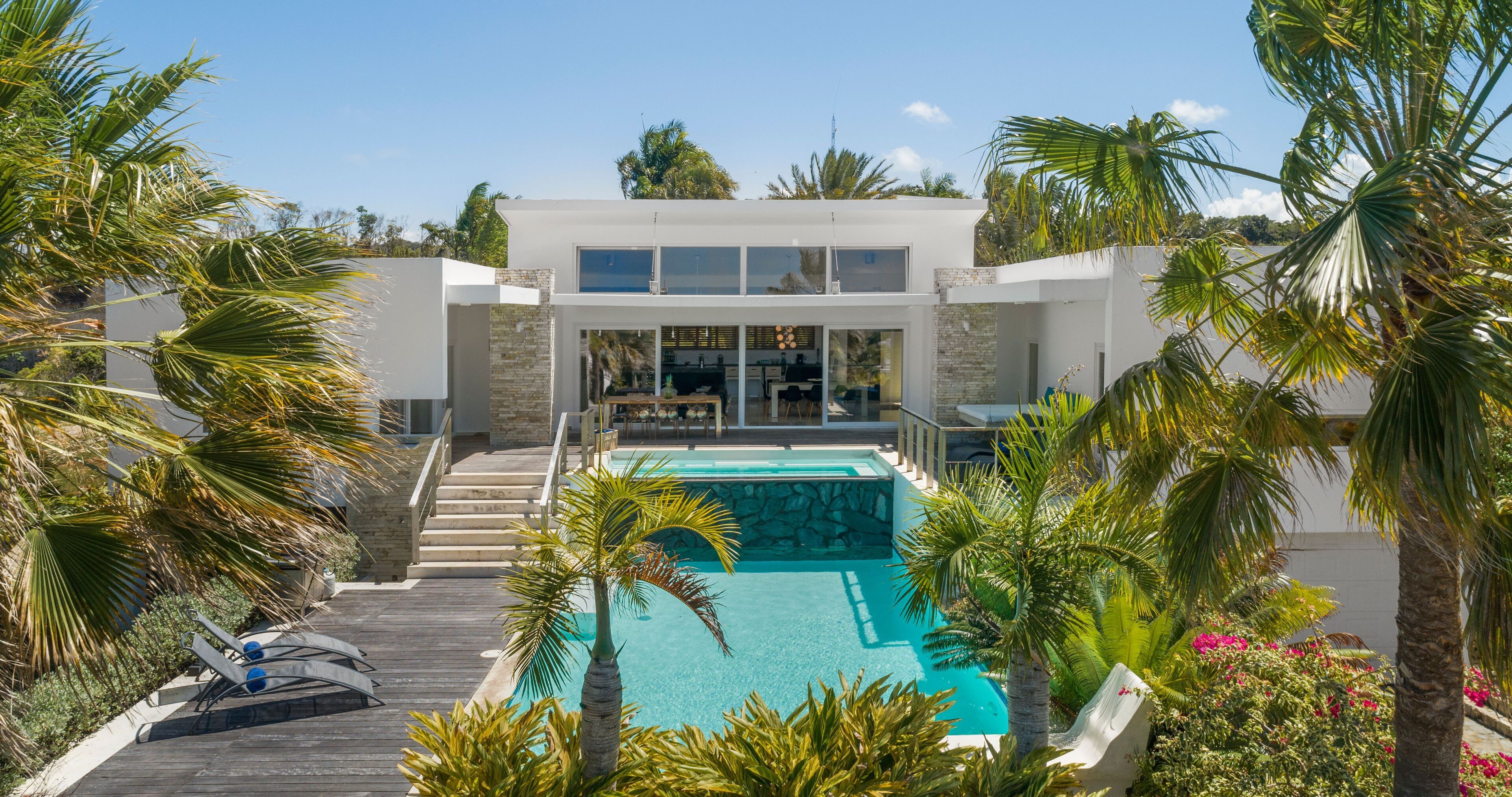 A modern house with a swimming pool, surrounded by palm trees and a wooden deck.