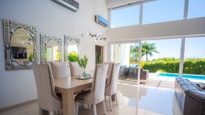 A modern dining area with a wooden table and chairs, large decorative mirrors, and a view of a swimming pool and greenery outside. - Villas Agua Dulce (Cabarete)